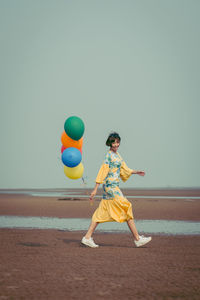 Full length portrait of young woman holding colorful balloons at beach