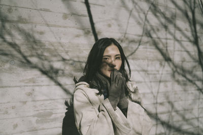 Portrait of young woman wearing warm clothing standing against wall