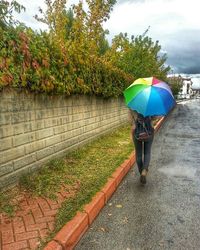 Rear view of woman walking on wet footpath during rainy season