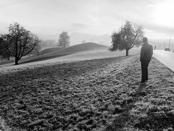 Rear view of man walking on field against sky