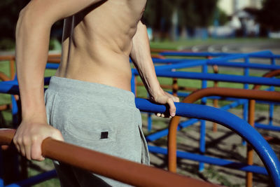 Midsection of shirtless man exercising on parallel bars