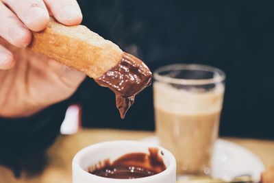 Close-up of hand holding creamy chocolate churro above table