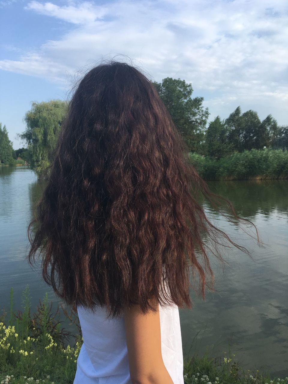 water, real people, one person, rear view, tree, leisure activity, lake, outdoors, day, sky, nature, standing, long hair, casual clothing, lifestyles, women, cloud - sky, young women, beauty in nature, young adult