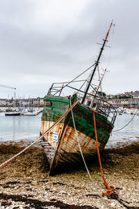 Fishing boat moored on beach against sky