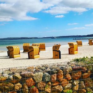 Deck chairs on beach against cloudy sky