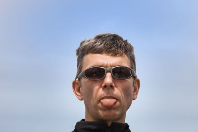 Portrait of man wearing sunglasses while sticking out tongue against clear sky
