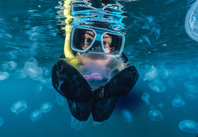 A woman in a black wetsuit is in the water with jellyfish. the jellyfish are floating around her