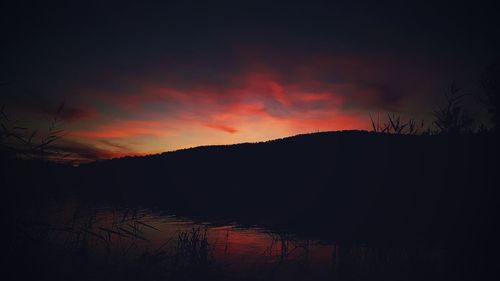 Silhouette trees by lake against sky at night