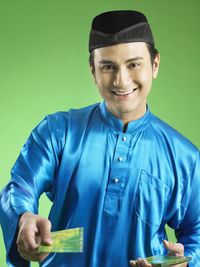 Portrait of man giving envelope against green background