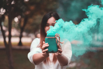 Woman holding jar emitting green smoke while standing outdoors
