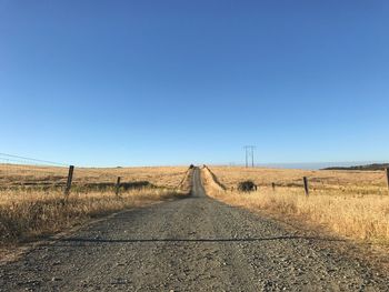 Road amidst field against clear blue sky