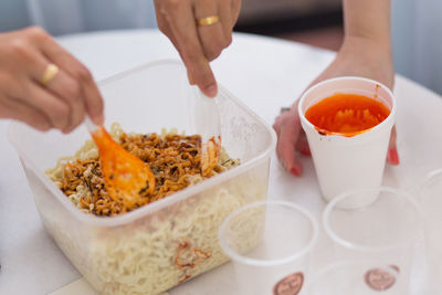 Cropped hands of friends preparing korean instant noodles on table