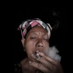 Portrait of man smoking against black background