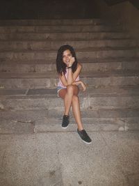 Portrait of smiling beautiful woman sitting on steps at night