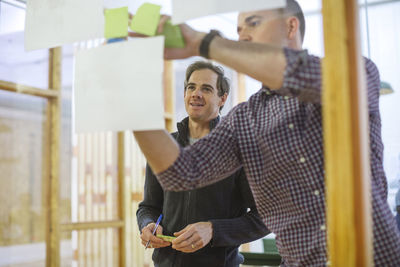 Businessmen sticking notes on glass in office