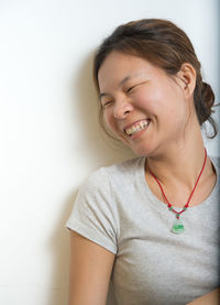 Portrait of a smiling young woman with eyes closed against wall