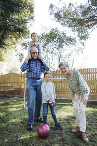 Portrait of happy grandparents with grandsons playing soccer at yard