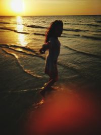 Girl on beach against sky during sunset