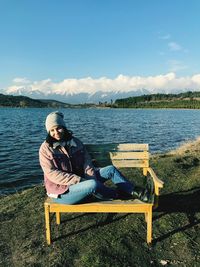 Portrait of woman sitting on bench against lake