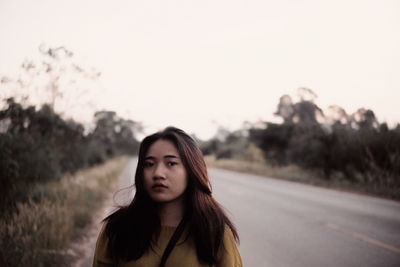 Portrait of beautiful young woman on road against sky