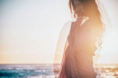 Double exposure of woman standing at beach against sky during sunset