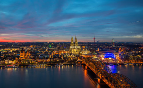 Illuminated bridge over river against sky at sunset