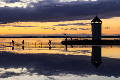 Silhouette built structure by sea against sky during sunset