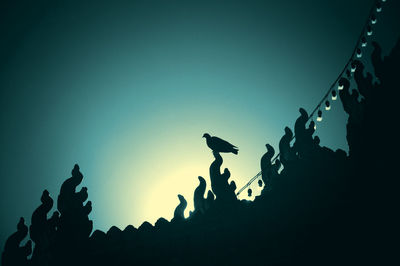 Low angle view of silhouette bird on temple roof against sky