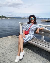 Portrait of woman sitting on bench against sea