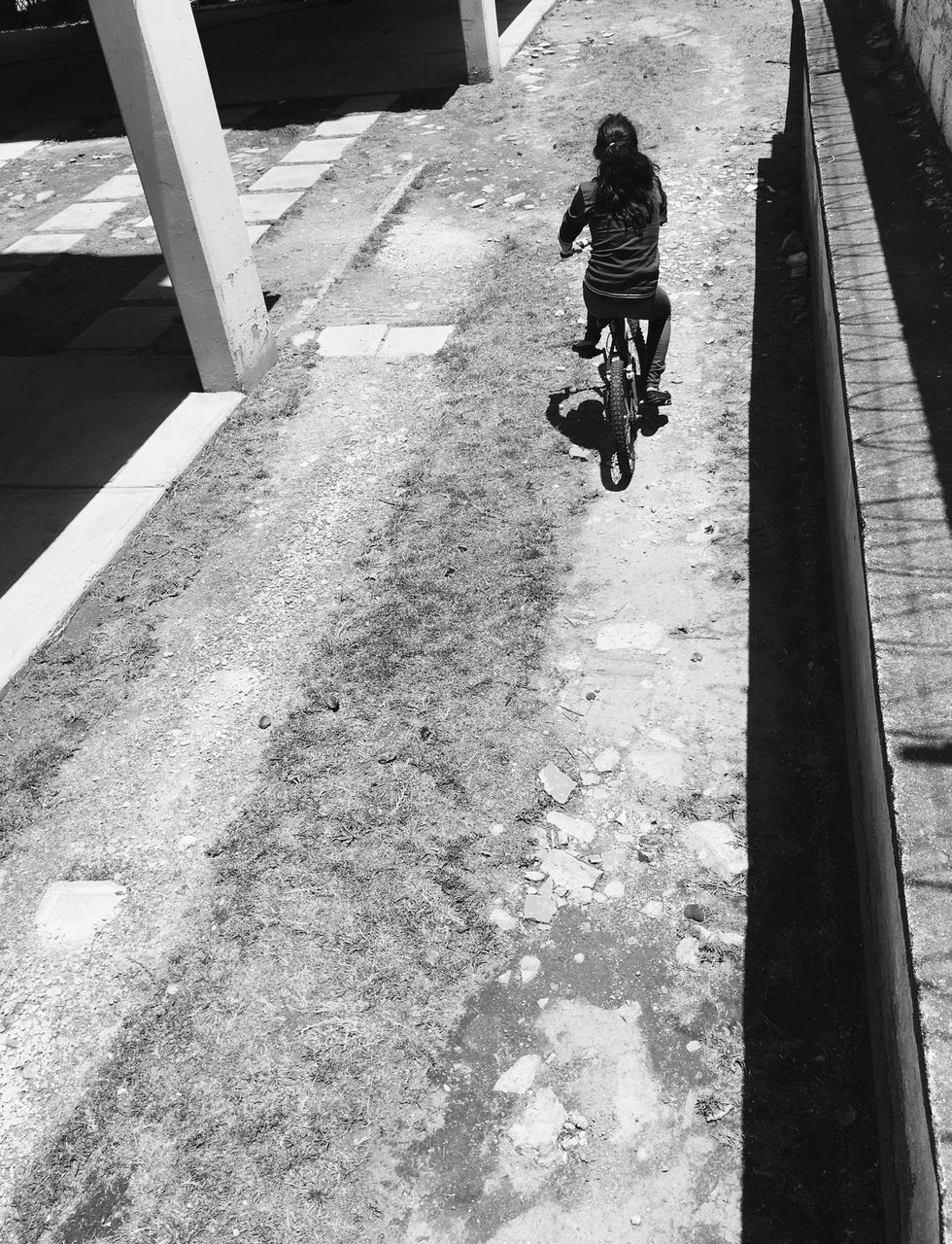 HIGH ANGLE VIEW OF MAN RIDING BICYCLE ON COBBLESTONE
