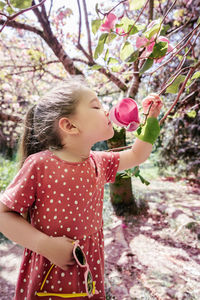 A girl in a pink polka dot dress holds a sprig of a blooming magnolia.