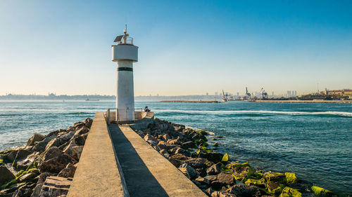 Lighthouse amidst sea and buildings against sky