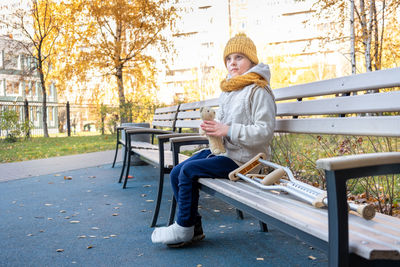 Kid walks in autumn park on crutches. child sitting on park bench and playing with toys. girl 