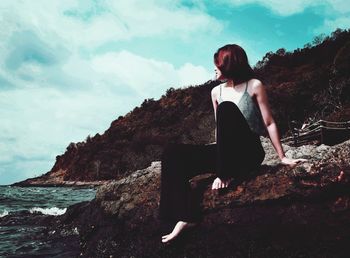 Woman sitting on rock against sky
