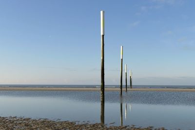 Wooden posts in lake against clear blue sky