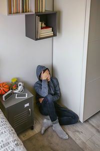 Side view of young woman sitting on suitcase at home