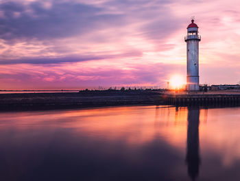 Lighthouse by sea against sky during sunset