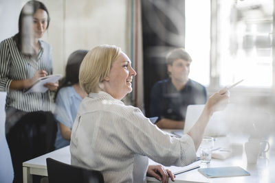 Smiling businesswoman pointing while sitting with colleagues in board room during meeting