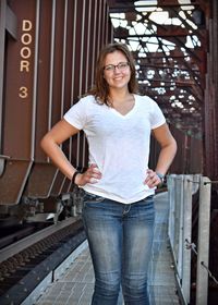 Portrait of smiling young woman with hands on hip standing on bridge