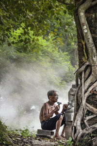 Shirtless senior man carving ganesha statue on field