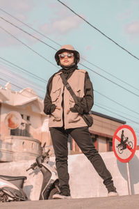 Low angle portrait of young woman standing against sky