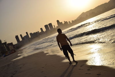 Rear view of man on beach against sky during sunset