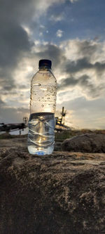 Glass of water bottle against sky during sunset