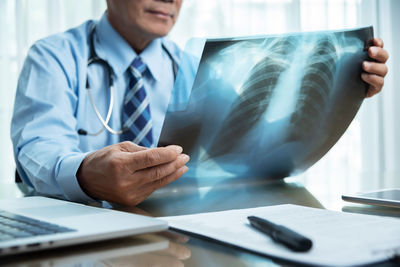 Midsection of doctor holding medical x-ray on table