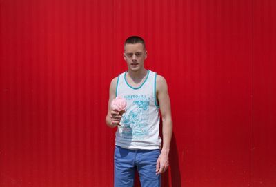 Portrait of young man standing against red wall