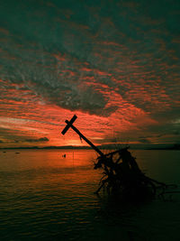 Silhouette fishing net on sea against sky during sunset