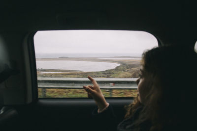 Girl pointing at sea from car window