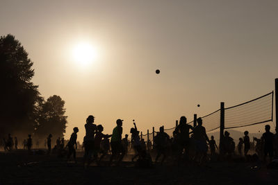 Silhouette people playing volleyball at beach during sunset