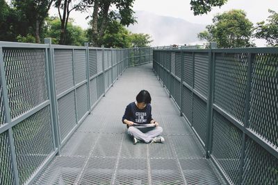 Full length of man sitting on railing against bridge