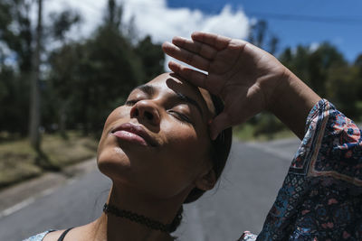 Close-up of young woman with eyes closed standing on road during sunny day